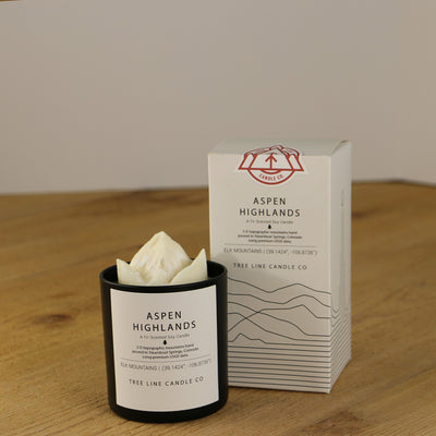 A white wax candle named Aspen Highlands is next to a white box with red and black lettering.