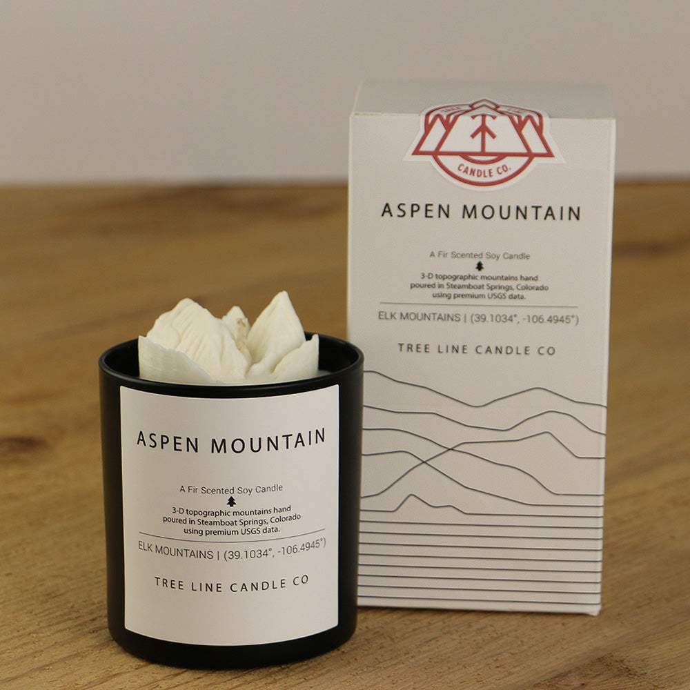 A white wax candle named Aspen Mountain is next to a white box with red and black lettering.