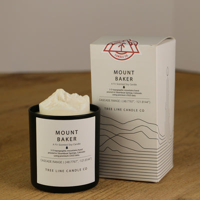 A white wax candle named Mount Baker is next to a white box with red and black lettering.