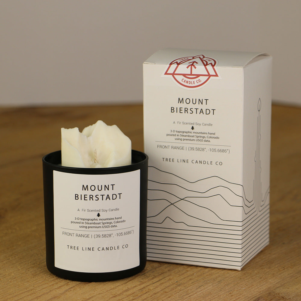 A white wax candle named Mount Bierstadt is next to a white box with red and black lettering.