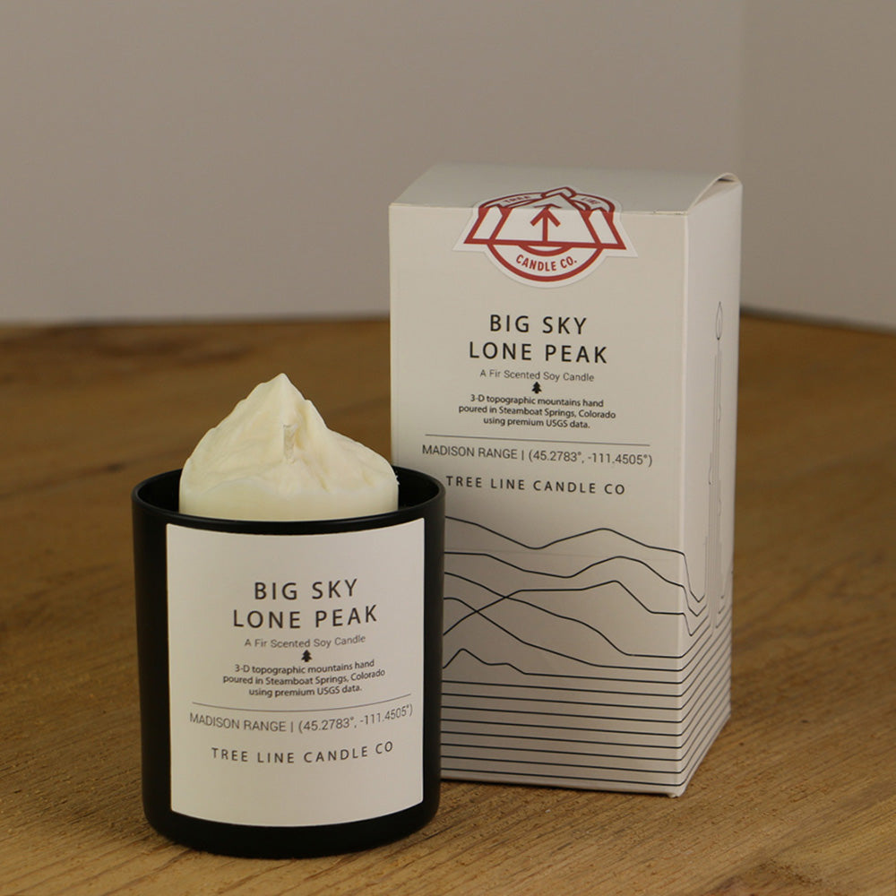 A white wax candle named Big Sky Lone Peak is next to a white box with red and black lettering.