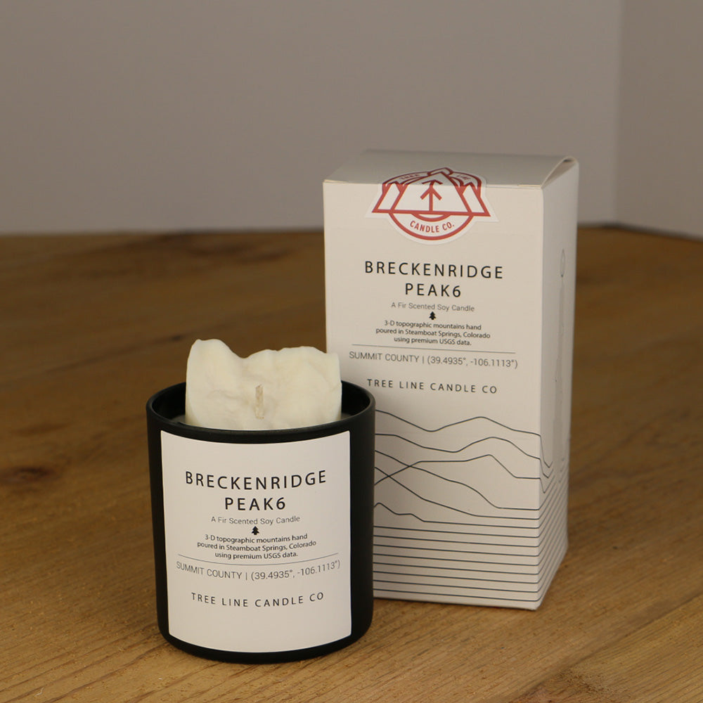 A white wax candle named Breckenridge Peak 6 is next to a white box with red and black lettering.