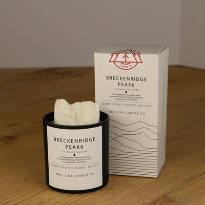 A white wax candle named Breckenridge Peak 6 is next to a white box with red and black lettering.