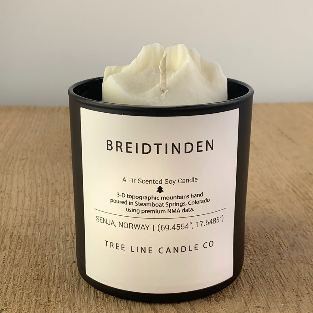 A white soy wax replica candle of Breidtinden in a round, black glass.
