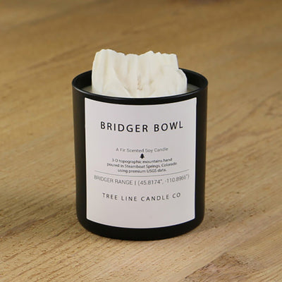  A white soy wax replica candle of Bridger Bowl mountain in a round, black glass.