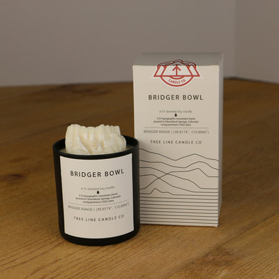 A white wax candle named Bridger Bowl is next to a white box with red and black lettering.