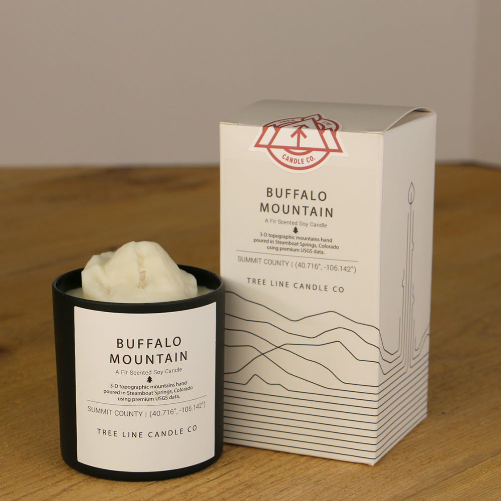 A white wax candle named Buffalo Mountain is next to a white box with red and black lettering.