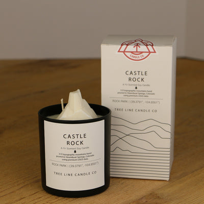 A white wax candle named Castle Rock is next to a white box with red and black lettering.