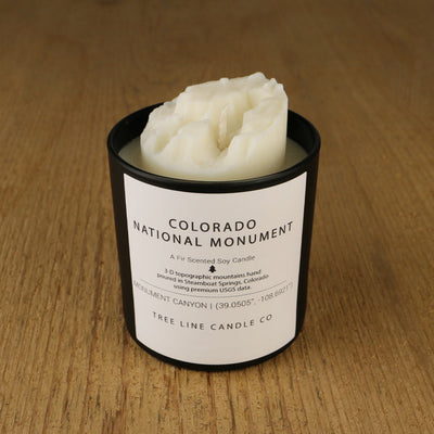 A white soy wax replica candle of Colorado National Monument in a round, black glass.
