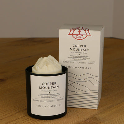 A white wax candle named Copper Mountain is next to a white box with red and black lettering.
