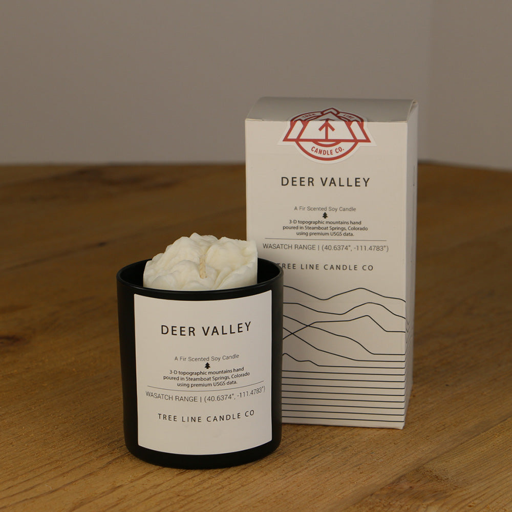 A white wax candle named Deer Valley is next to a white box with red and black lettering.