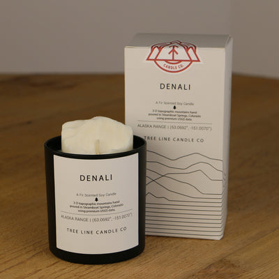 A white wax candle named Denali is next to a white box with red and black lettering