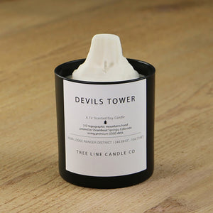 A white soy wax replica candle of Devils Tower in a round, black glass.