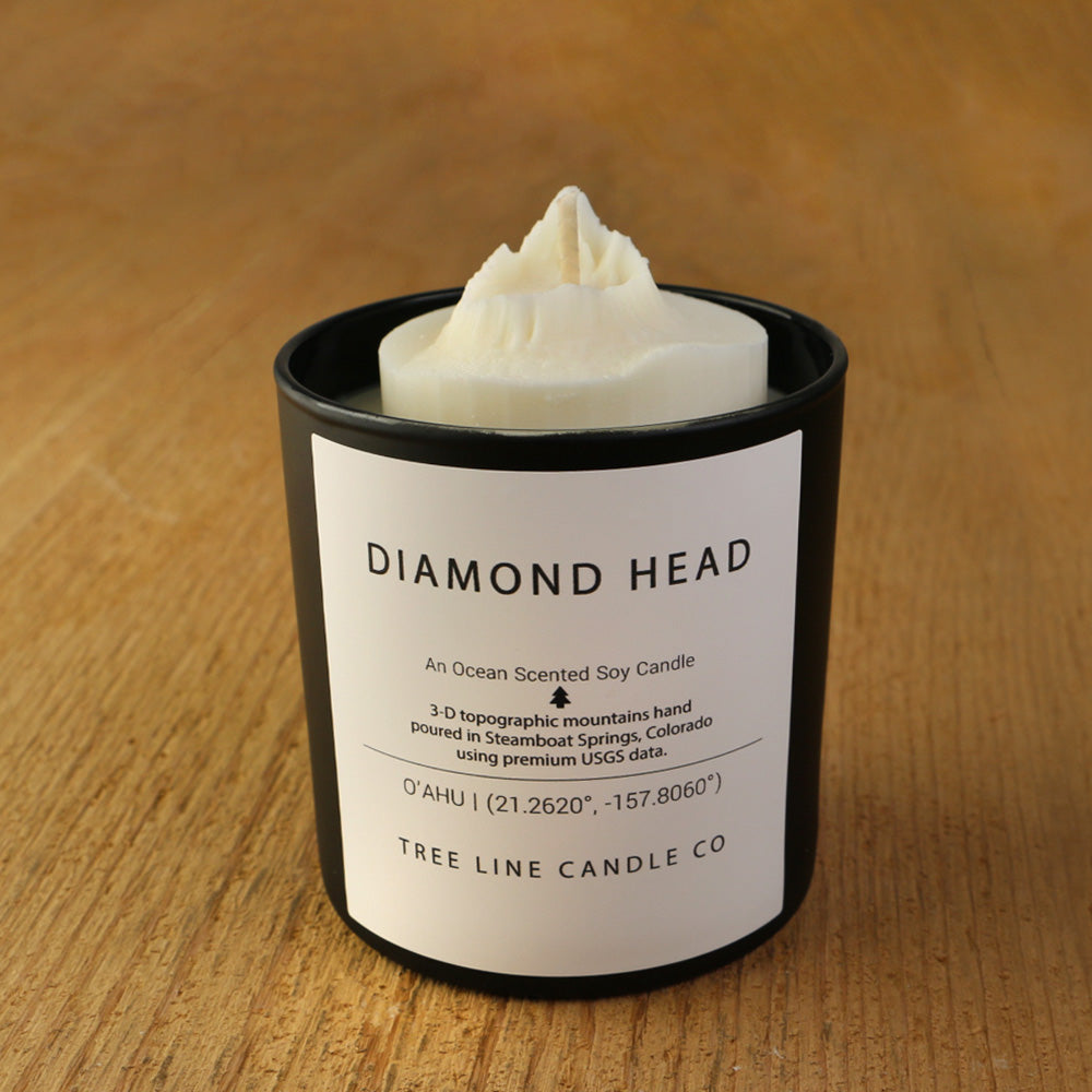 A white soy wax replica candle of Diamond Head in a round, black glass.