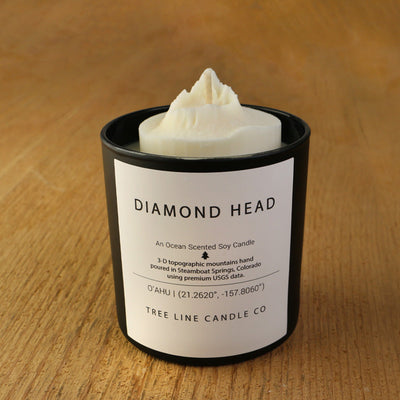 A white soy wax replica candle of Diamond Head in a round, black glass.
