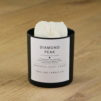 A white soy wax replica candle of Diamond Peak in a round, black glass.