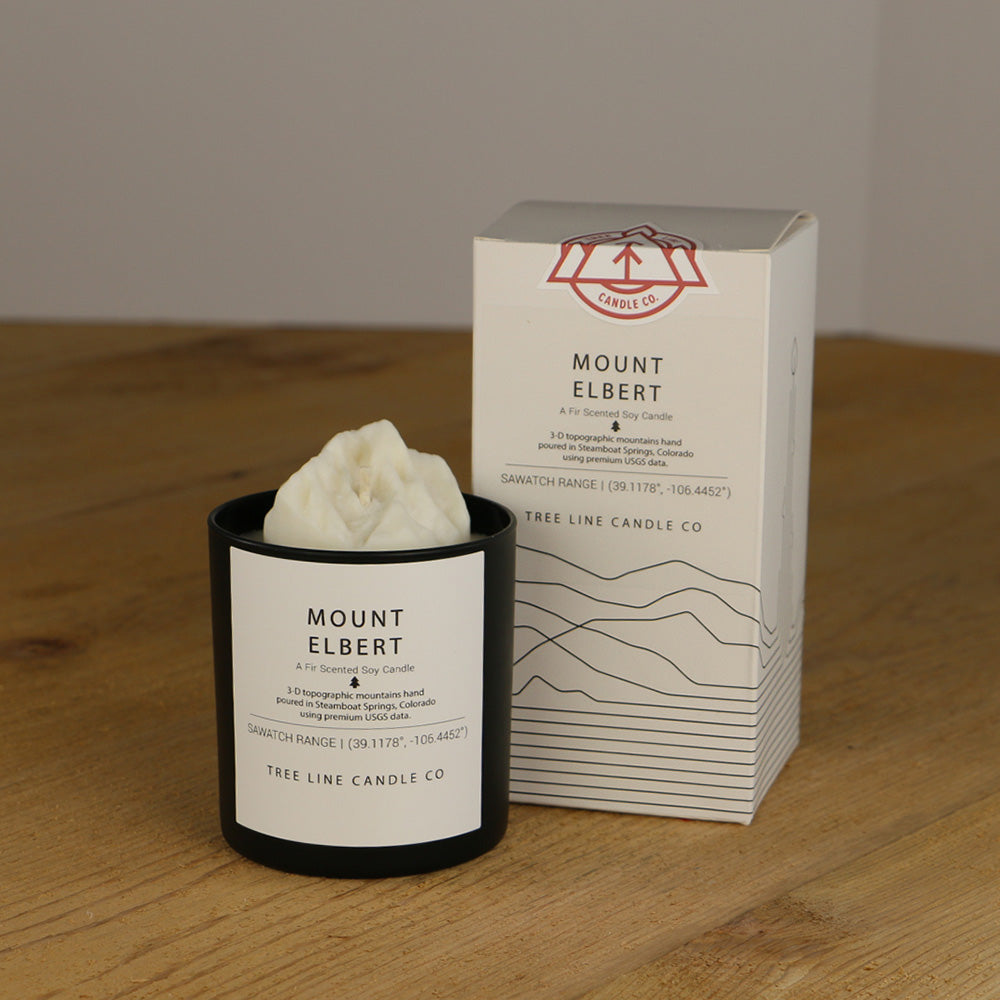 A white wax candle named Mount Elbert is next to a white box with red and black lettering.