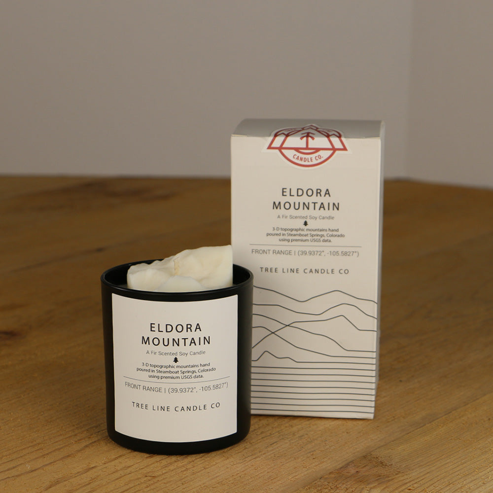 A white wax candle named Eldora Mountain is next to a white box with red and black lettering.