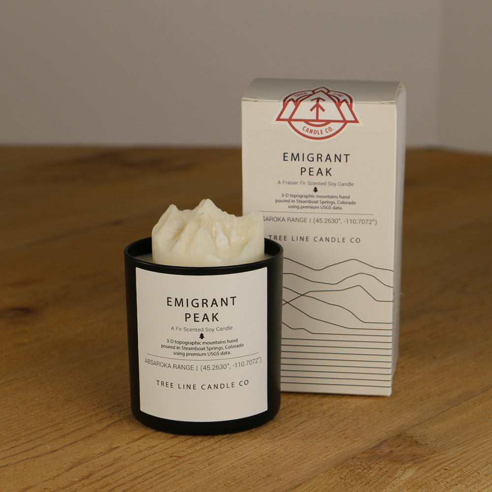 A white wax candle named Emigrant Peak is next to a white box with red and black lettering.