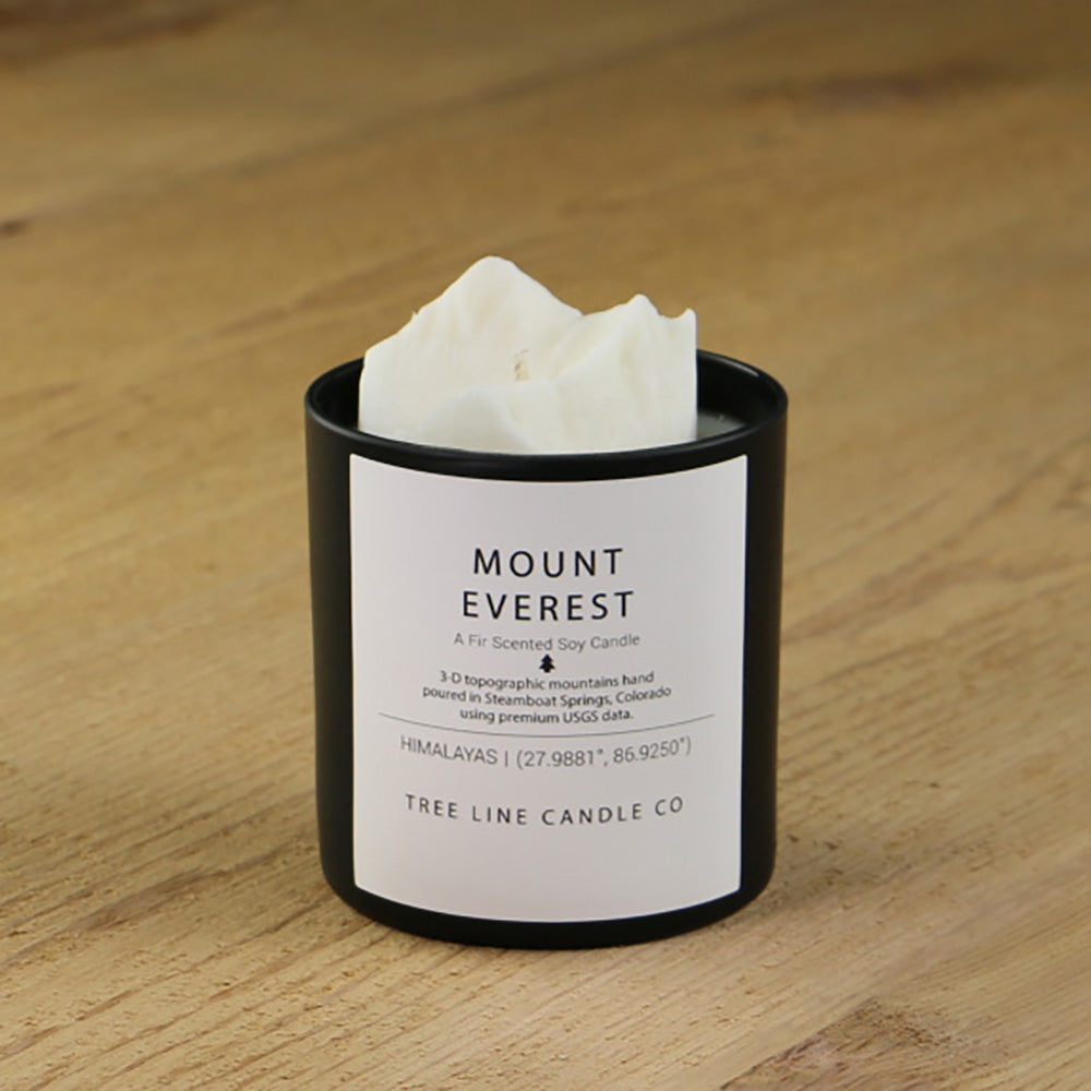A white soy wax replica candle of Mount Everest in a round, black glass.