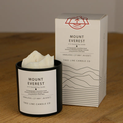 A white wax candle named Mount Everest is next to a white box with red and black lettering.