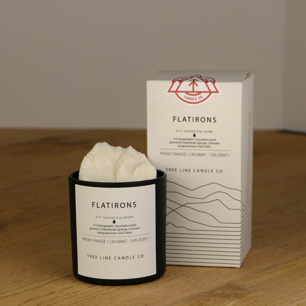 A white wax candle named Flatirons is next to a white box with red and black lettering.