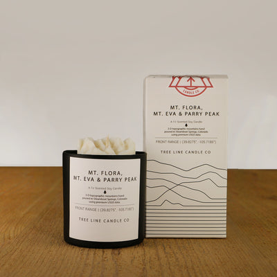 A white wax candle named  Mt. Flora, Mt. Eva & Parry Peak is next to a white box with red and black lettering.