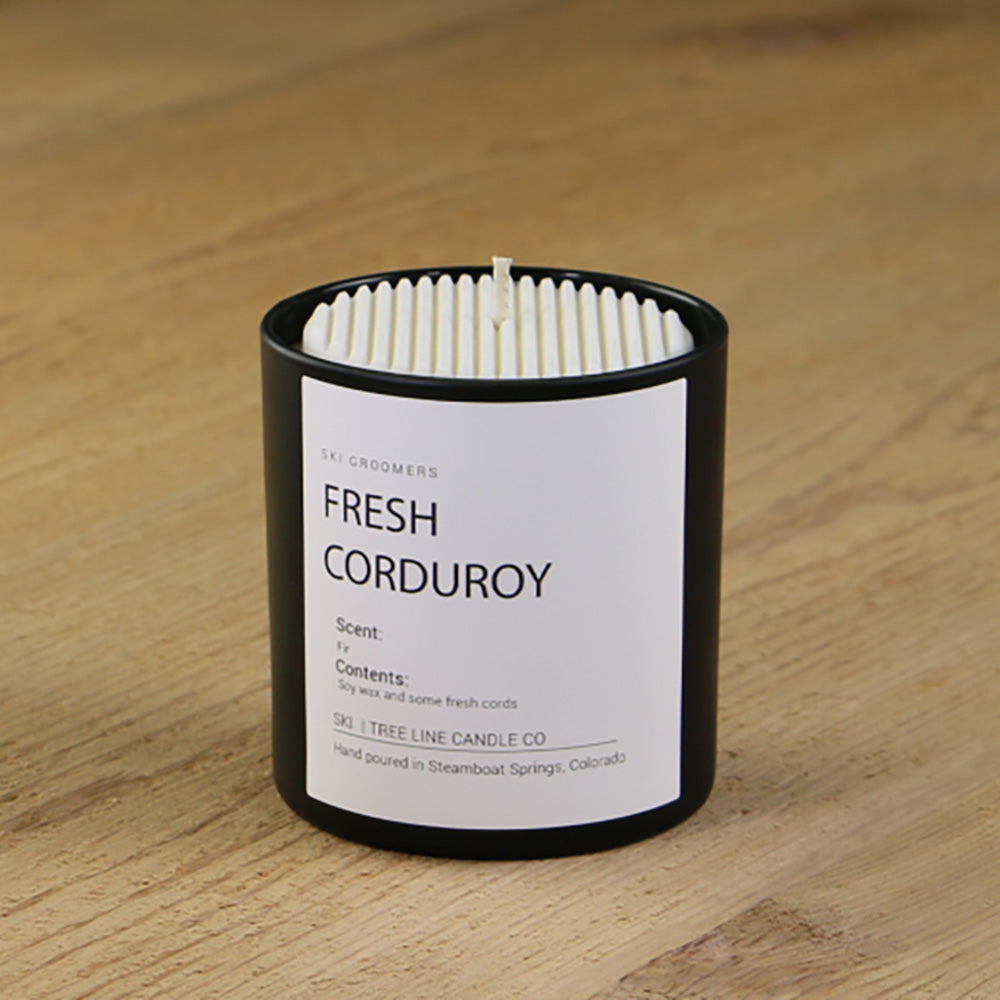  A white soy wax replica candle of Fresh Corduroy in a round, black glass.