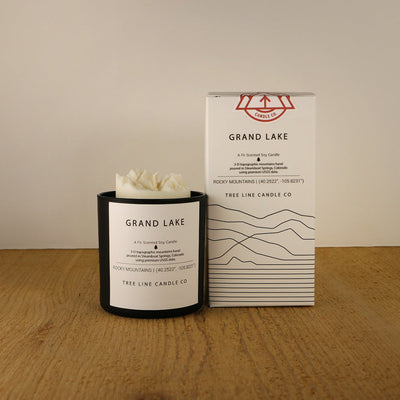 A white wax candle named Grand Lake is next to a white box with red and black lettering.