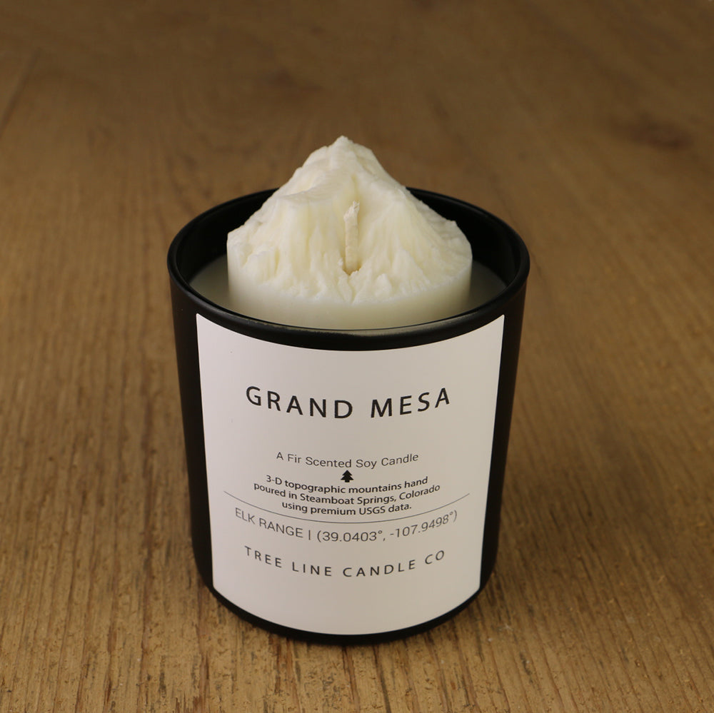 A white soy wax replica candle of Grand Mesa in a round, black glass.