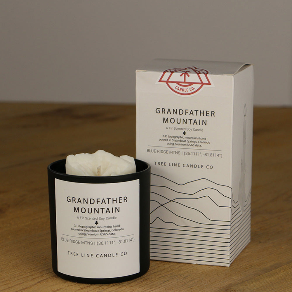 A white wax candle named Grandfather Mountain is next to a white box with red and black lettering.
