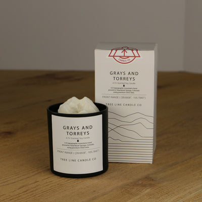 A white wax candle named Grays and Torreys is next to a white box with red and black lettering.