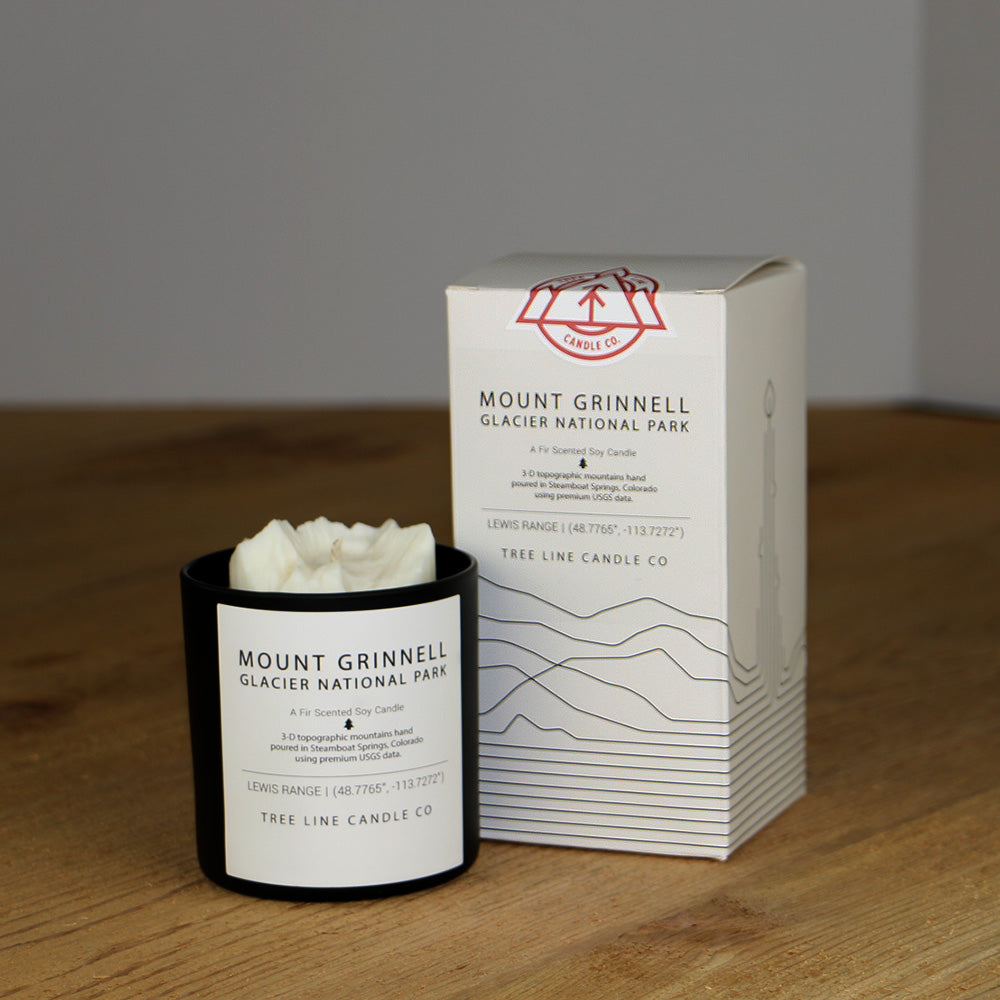 A white wax candle named Mount Grinnell is next to a white box with red and black lettering.