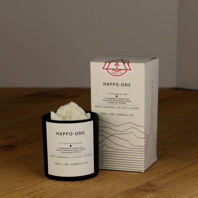 A white wax candle named Happo-One mountain is next to a white box with red and black lettering.