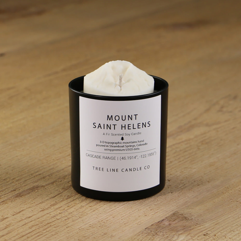 A white soy wax replica candle of Mount Saint Helens in a round, black glass.