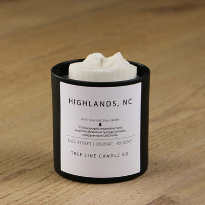  A white soy wax replica candle of Highlands  in a round, black glass.
