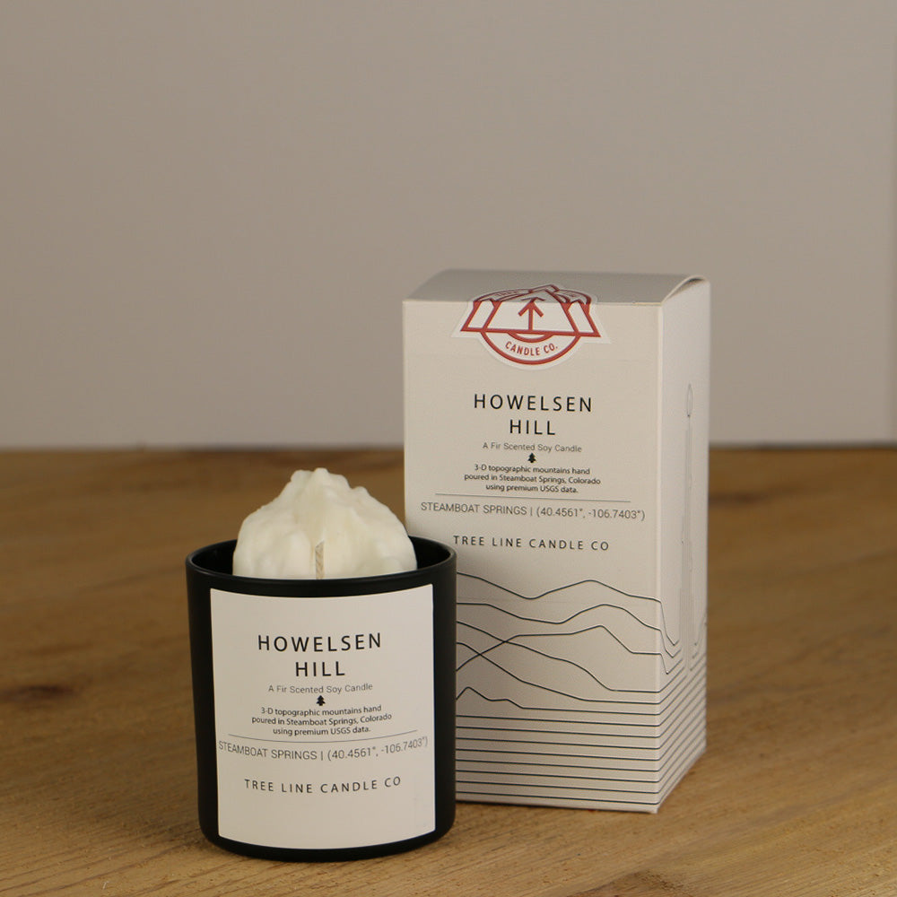 A white wax candle named Howelsen Hill is next to a white box with red and black lettering.