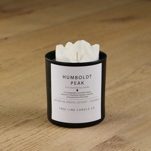 A white soy wax replica candle of Humboldt Peak in a round, black glass.