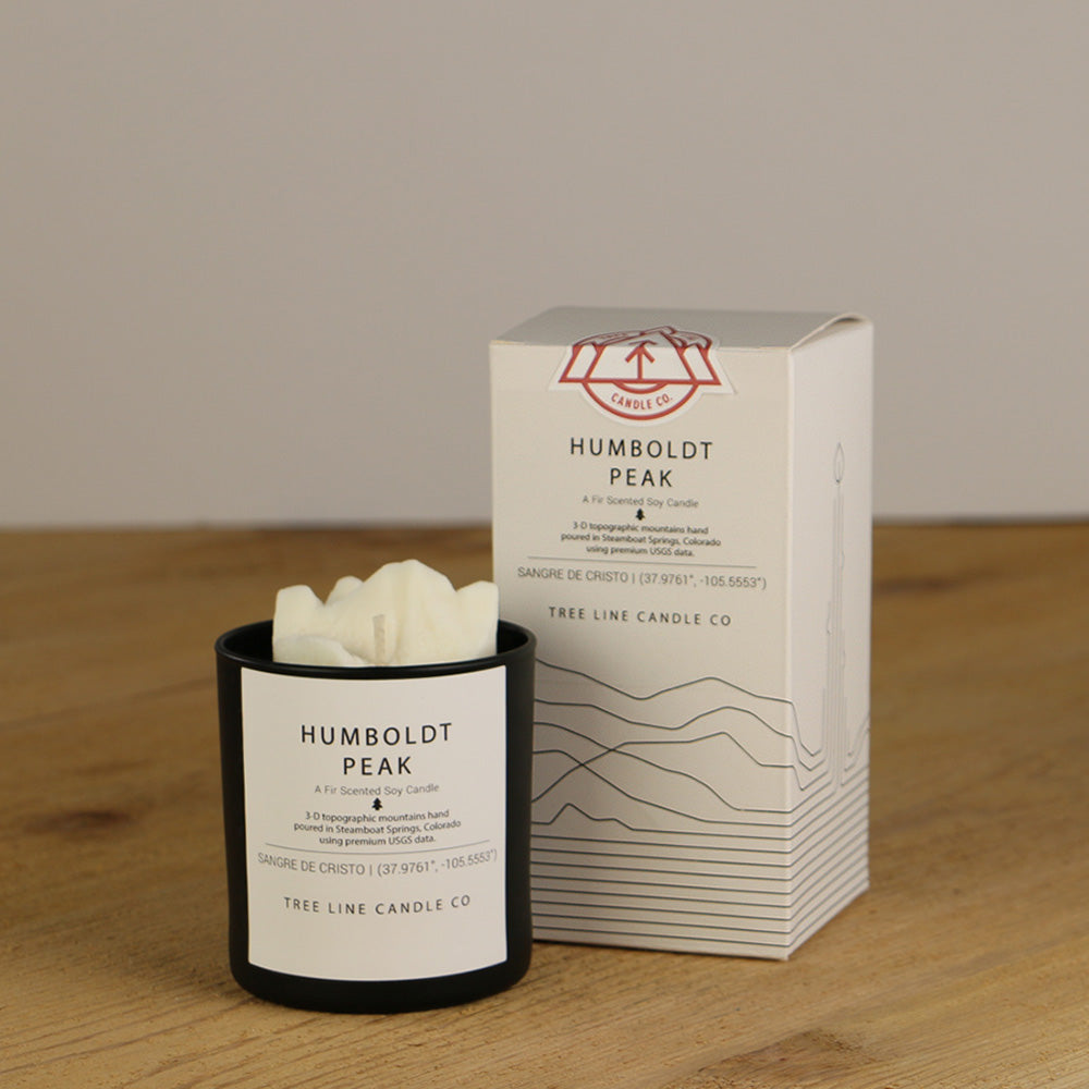 A white wax candle named Humboldt Peak is next to a white box with red and black lettering.