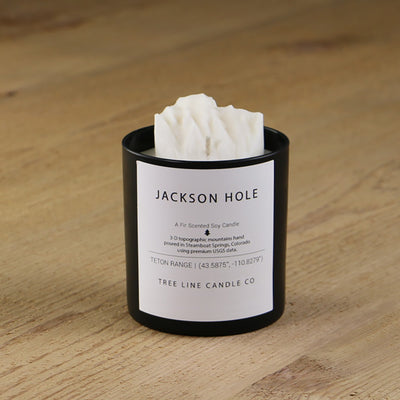 A white soy wax replica candle of Jackson Hole summit in a round, black glass.