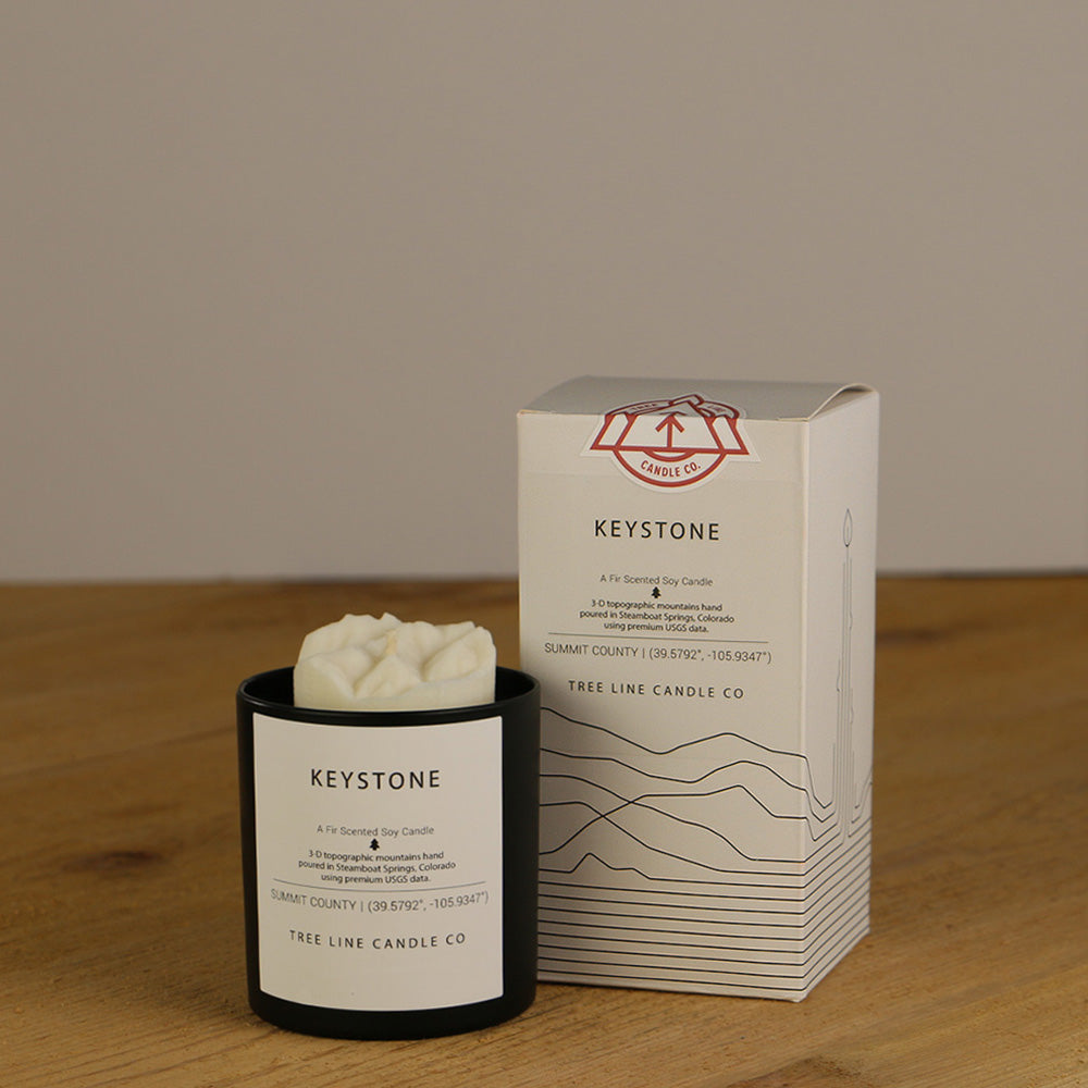 A white wax candle named Keystone is next to a white box with red and black lettering.