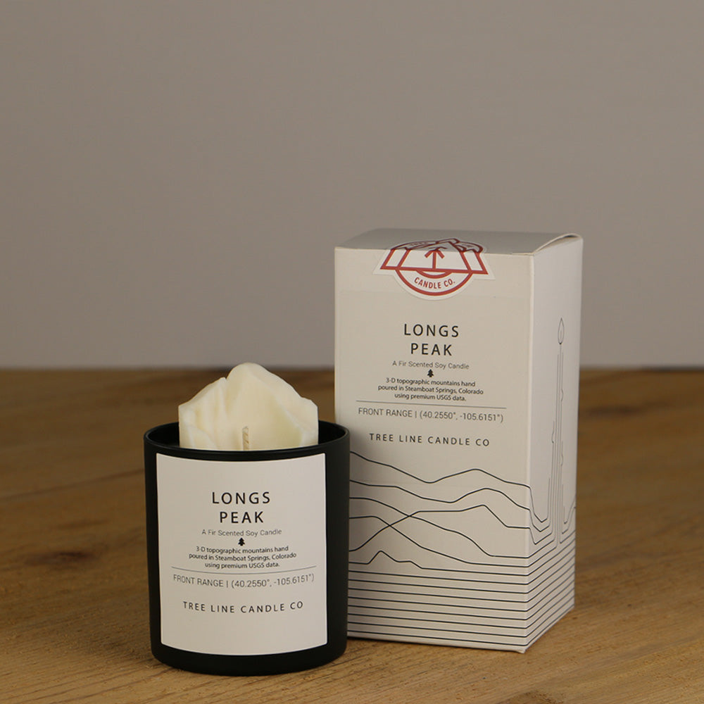 A white wax candle named Longs Peak is next to a white box with red and black lettering.