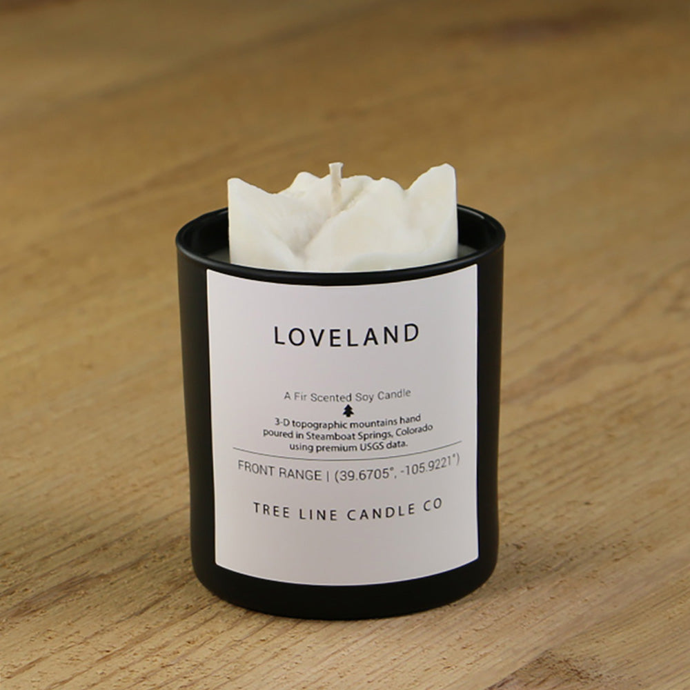 A white soy wax replica candle of Loveland summit in a round, black glass.