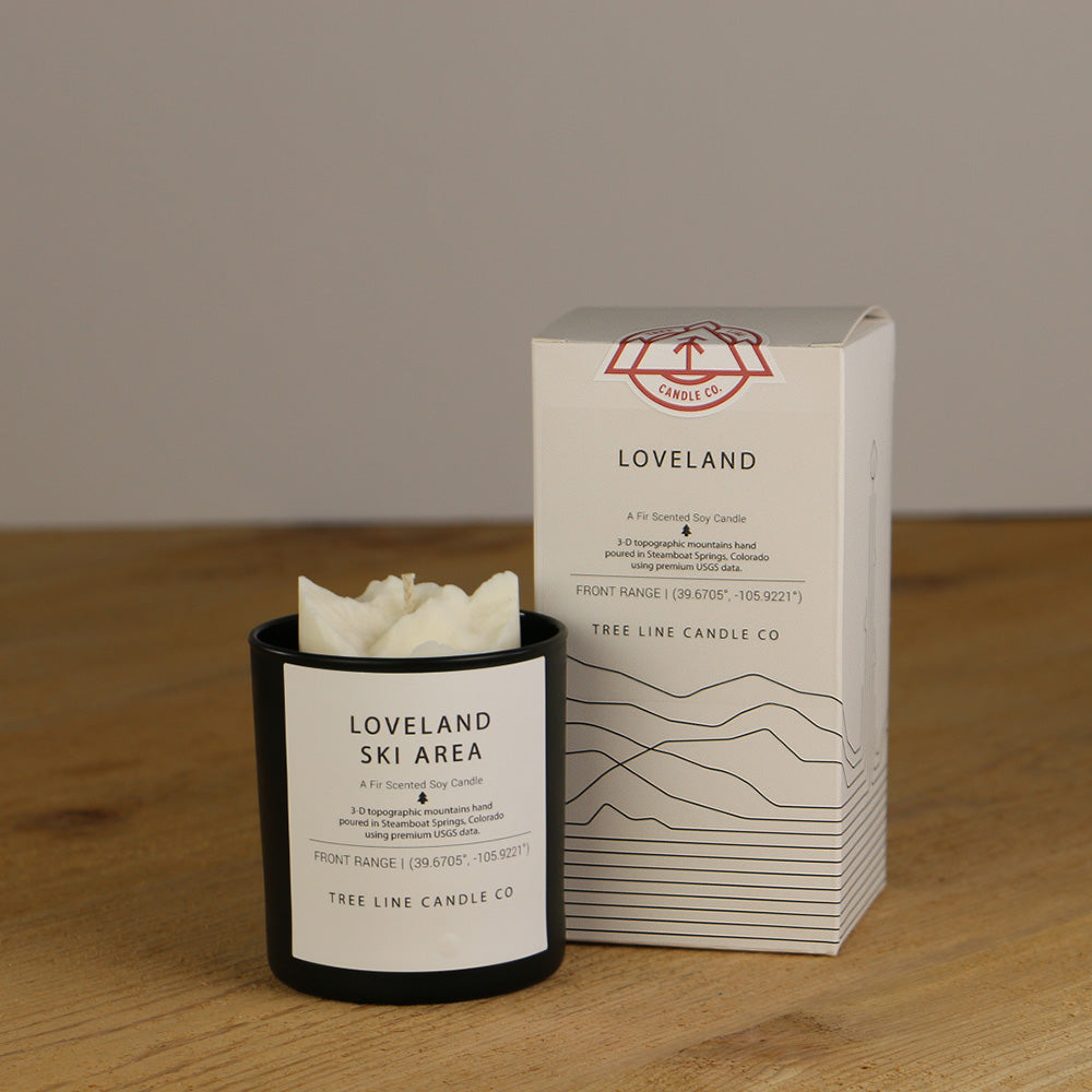 A white wax candle named Loveland is next to a white box with red and black lettering.