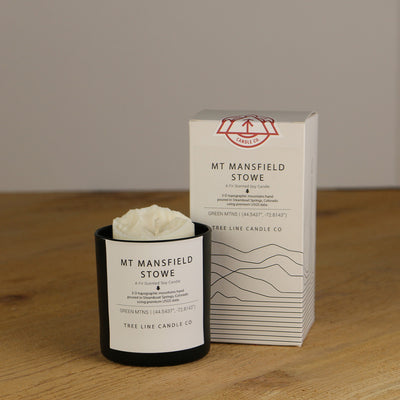 A white wax candle named Mt. Mansfield Stowe is next to a white box with red and black lettering.