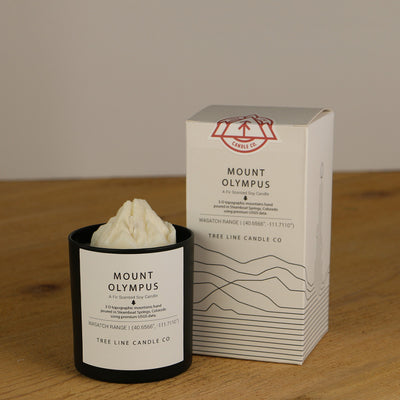 A white wax candle named Mount Olympus is next to a white box with red and black lettering.