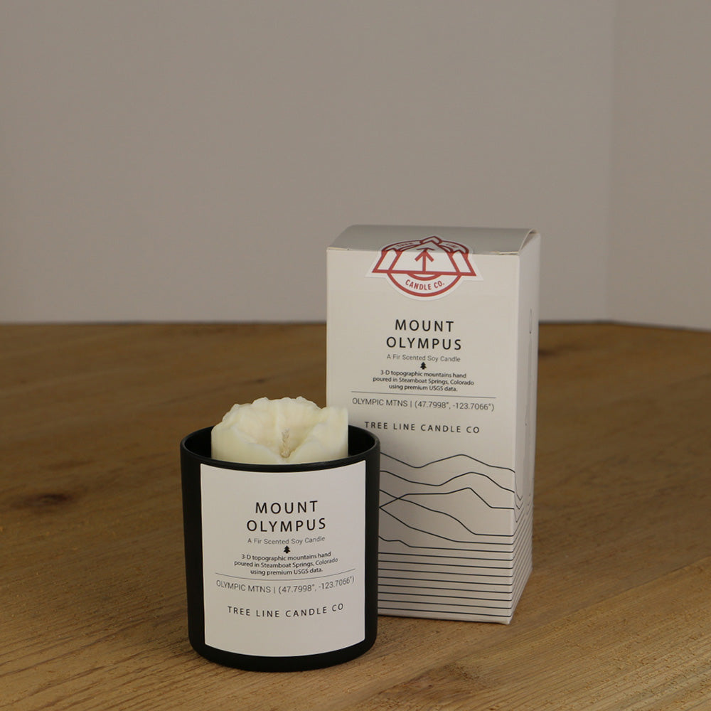 A white wax candle named Mount Olympus is next to a white box with red and black lettering.
