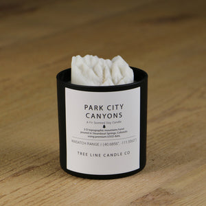 A white soy wax replica candle of Park City Canyons in a round, black glass.