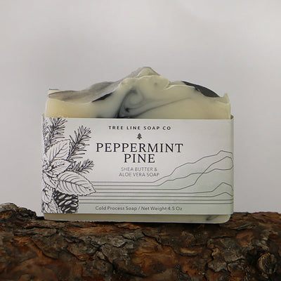 A single bar of Peppermint Pine soap sits on a log with dark bark.