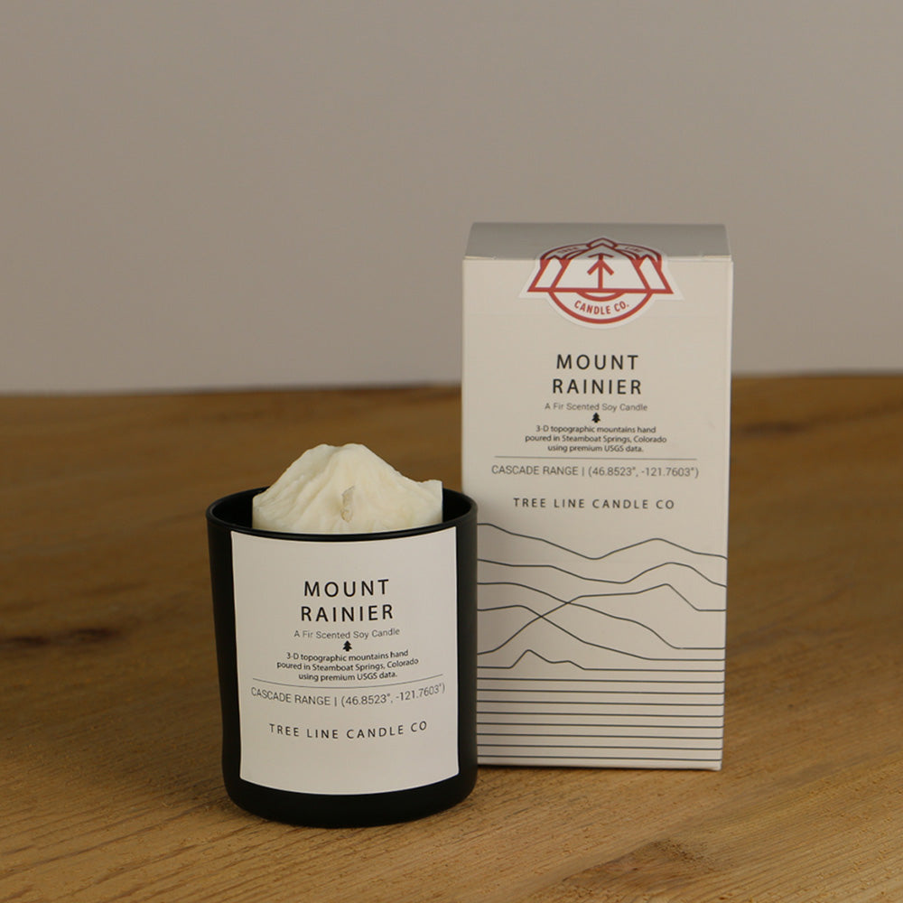 A white wax candle named Mount Rainier is next to a white box with red and black lettering.